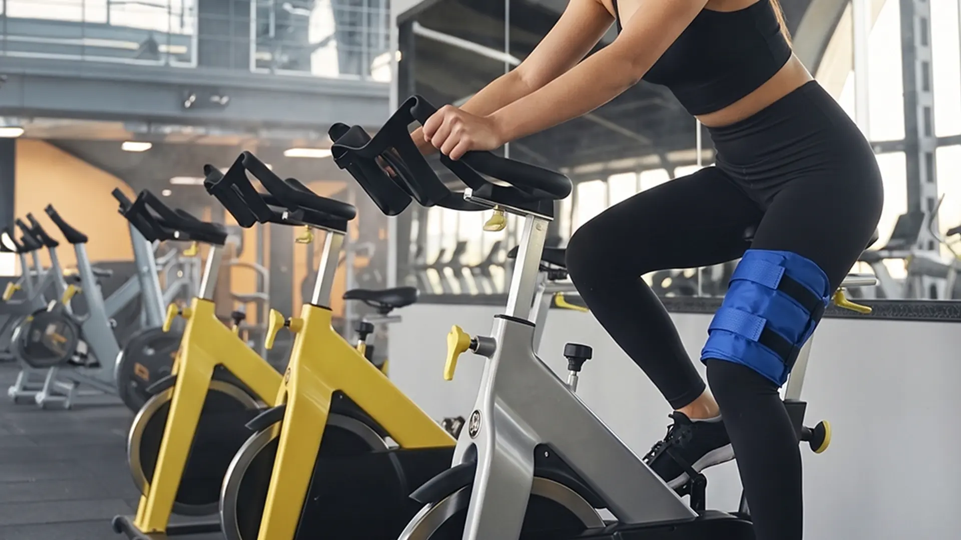 Mujer pedaleando en una bicicleta de spinning con una compresa Practiko's sujeta a la rodilla